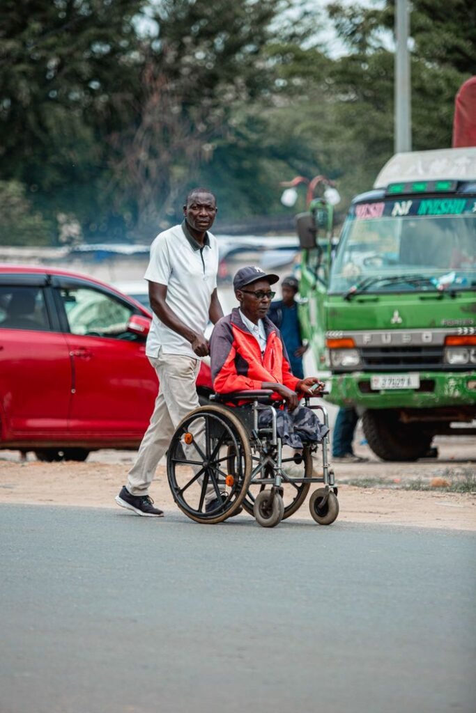 A loving father pushing his son in a wheelchair along a city road, surrounded by vehicles.