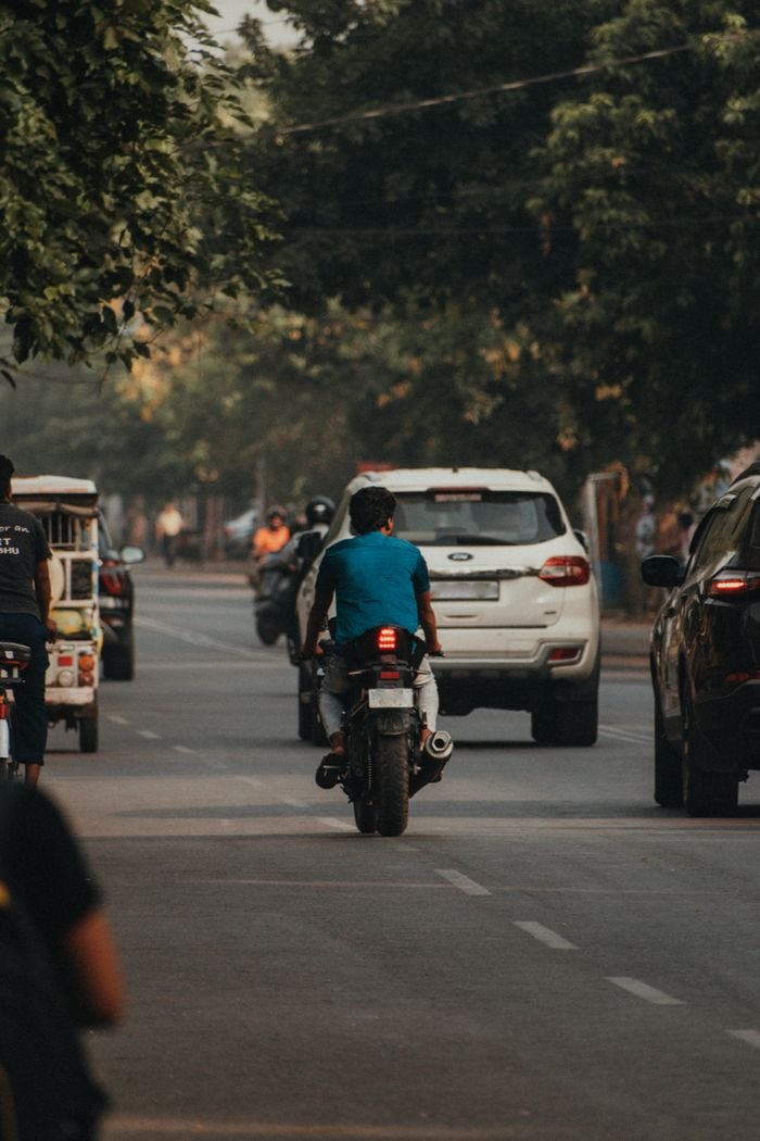 Motorcyclist riding through a busy urban street accompanied by cars and trees.
